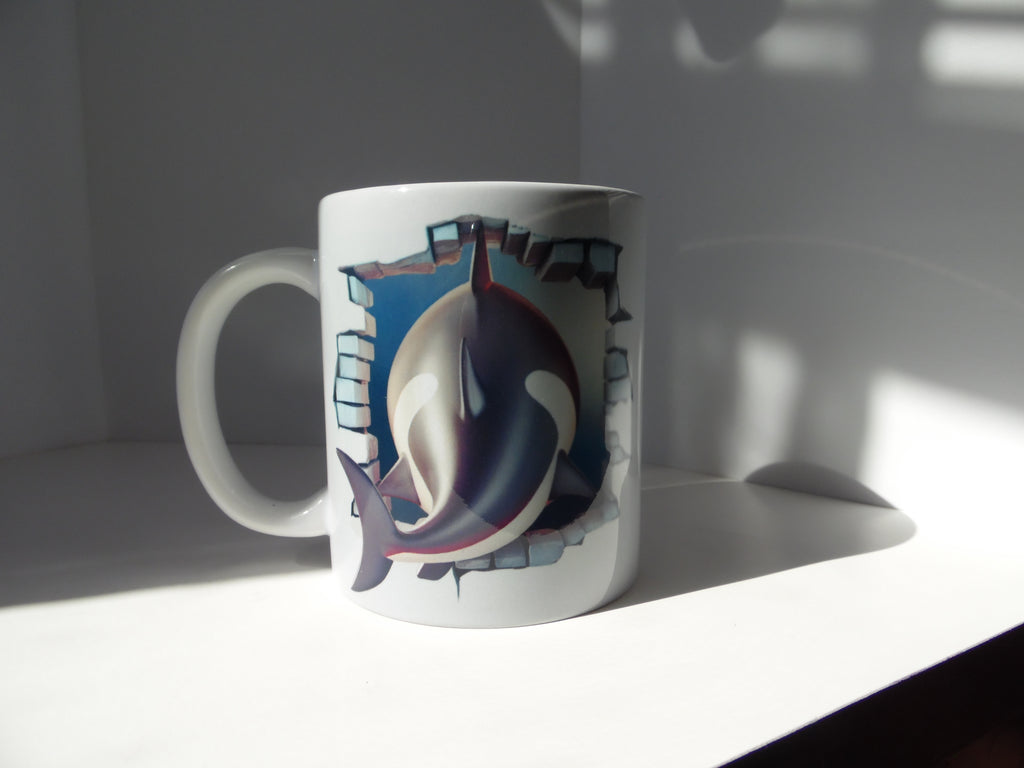 Reverse view of white ceramic mug showing orca body and tail against a blue background